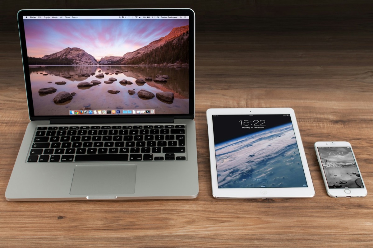 A laptop, tablet, and smartphone with screens on, placed together on a wooden desk